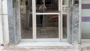 A building entrance with a glass door, a number sign above, and a metal gate to the right.