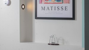 Una obra enmarcadas de 'La ventana abierta' de Matisse, una pequeña escultura de metal y un cojín verde sobre un sofá blanco.