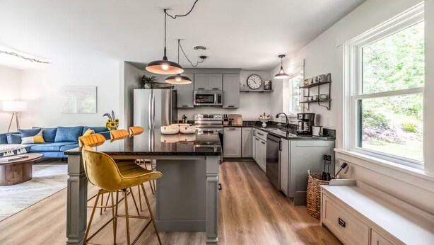 Una cocina moderna con una isla central, taburetes de bar, iluminación colgante y vistas al exterior.