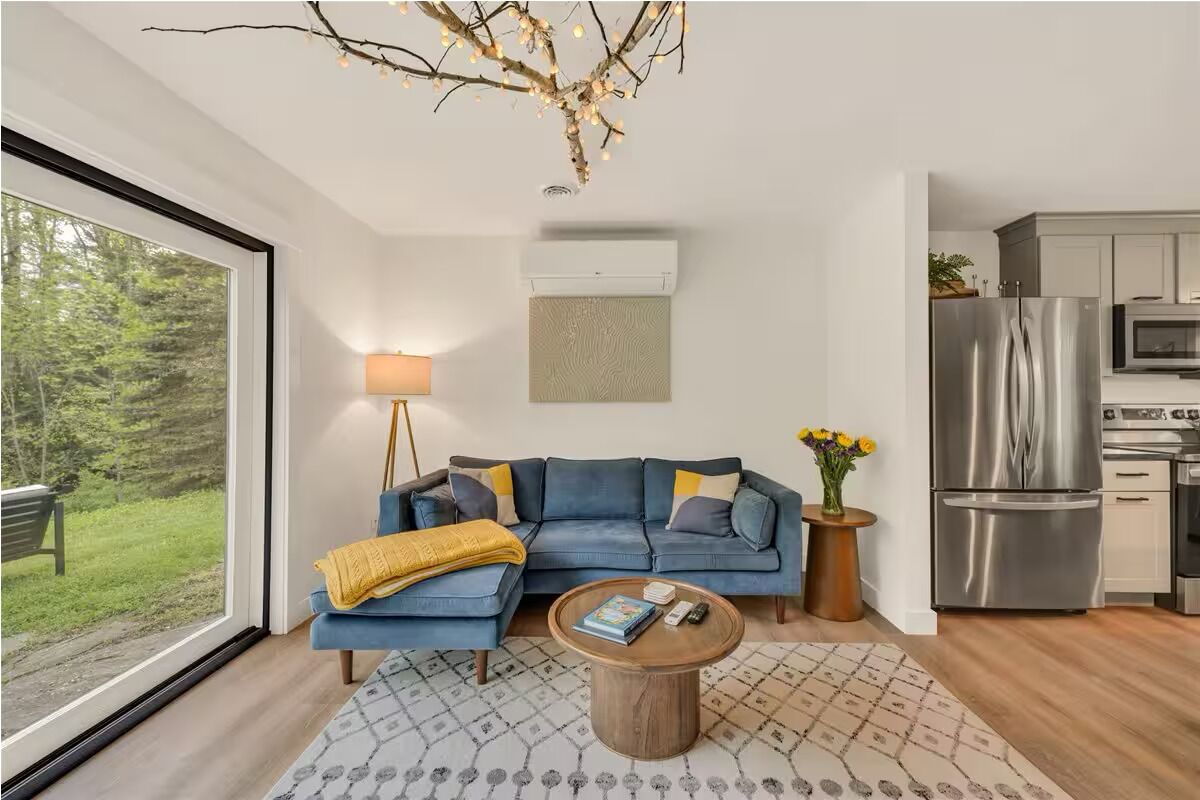 Een moderne woonkamer met een bank, salontafel en uitzicht op een bos.