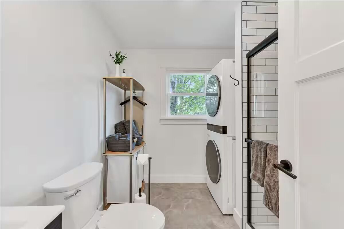 A compact laundry room with a washing machine, a drying rack, and a small window.