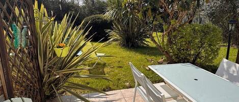 Un patio con mesa y sillas, rodeado de un jardín con diversas plantas y una valla de madera.
