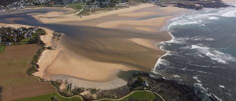 Vista aérea de uma área costeira com uma praia de areia, um pequeno povoado e um trecho de costa rochosa.