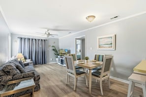 Ein Wohnzimmer mit einer Couch, einem Esstisch mit Stühlen, einem Deckenventilator und einem Fernseher.