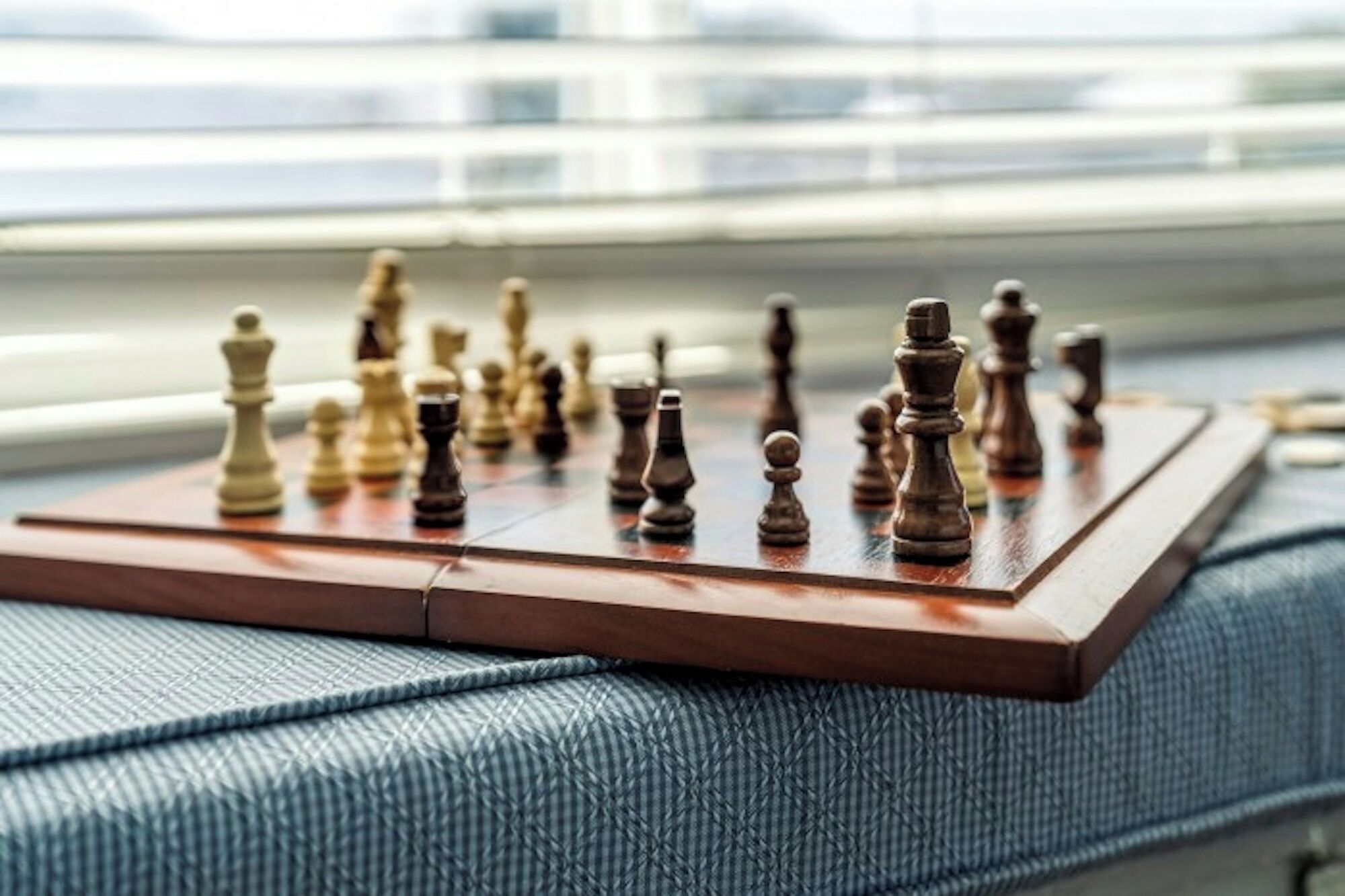 A chessboard on a wooden table near a window with blinds.