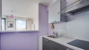 A modern kitchen with a built-in oven, a stainless steel sink, and a window overlooking a cityscape. - Spacious Studio 2P - Near La Defense (Courbevoie)