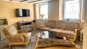A living room with a sofa, chairs, a coffee table, a TV, and a window with a plant. - Holiday Home in Konz (Konz)