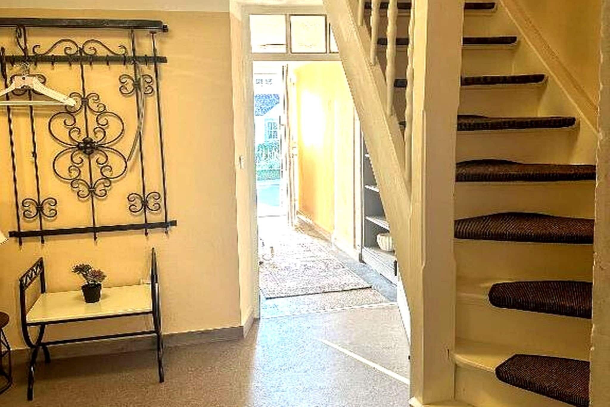 Eine Treppe mit Handlauf, ein Sessel mit Topfpflanze und ein dekoratives Metallobjekt an der Wand.