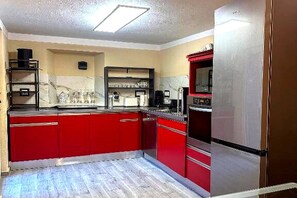 A kitchen with red cabinets, a stainless steel refrigerator, and a microwave.