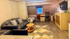 A compact room with a sofa, a small round table, a desk with a chair, a television, and a cabinet. - Gemütliche Wohnung in Konz an der Mosel (Konz)