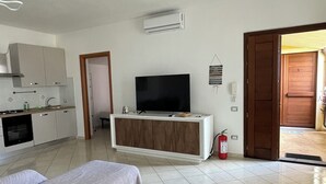 Una sala moderna con sofá, televisión sobre un mueble de madera, área de cocina con armarios y extintor.