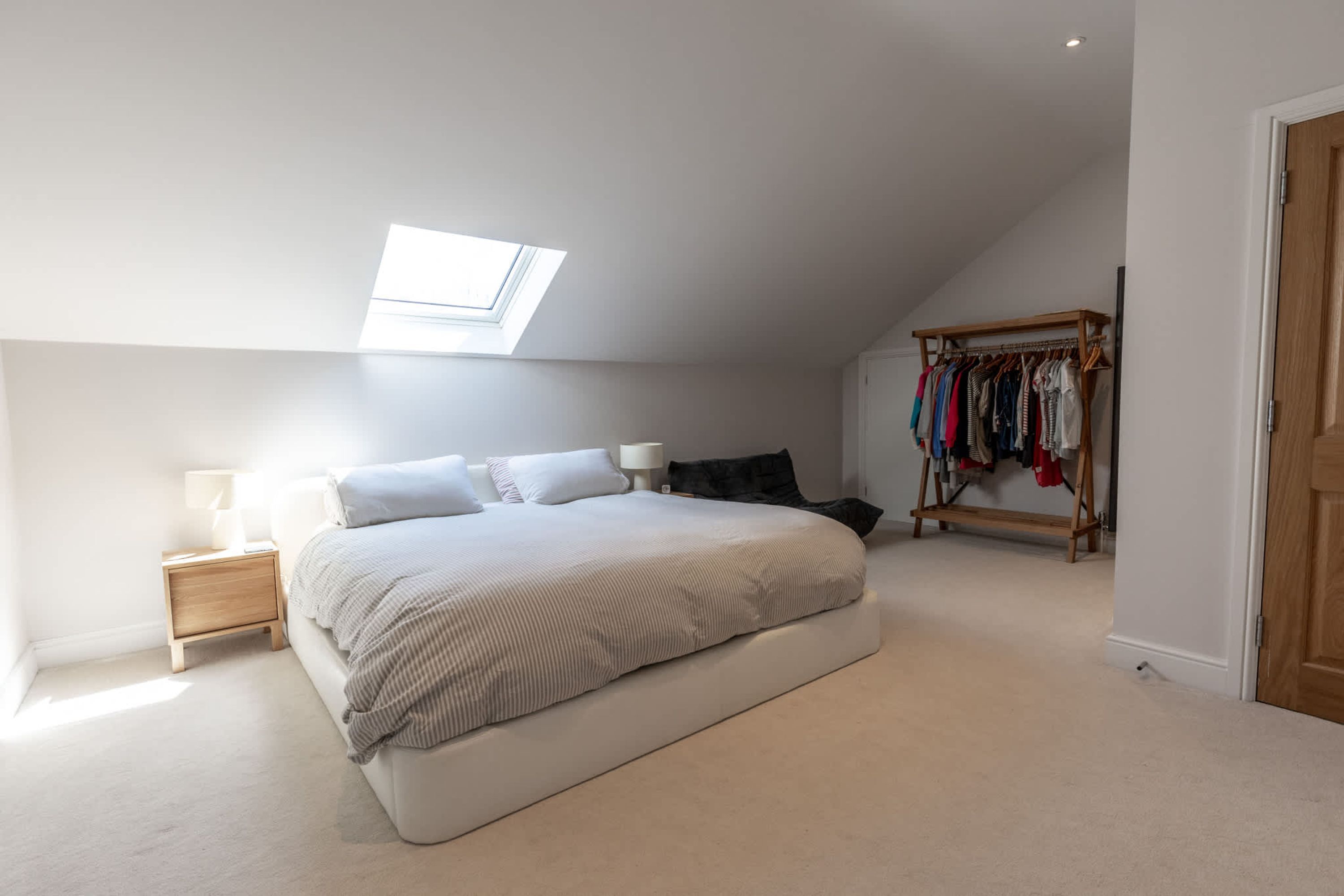 A bedroom with a skylight, a bed, a nightstand, a closet, and a door.