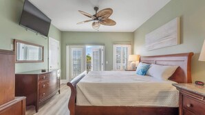 A bedroom with a bed, a ceiling fan, a TV, a dresser, and a window with blinds. - Coastal Cabana, an island escape (Carolina Beach)