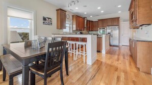 A kitchen with wooden cabinets, a dining area with a table and chairs, and a view of the outdoors. - Coastal Cabana, an island escape (Carolina Beach)