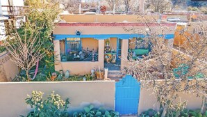 A residential building with a blue gate, a small garden with cacti, and a balcony with a table and chairs.