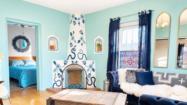 A room with a blue sofa, a patterned rug, a wooden coffee table, and a fireplace with blue and white decor.