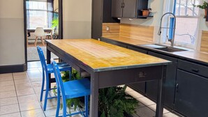 A kitchen with a wooden table, blue chairs, black cabinets, and a window with plants.