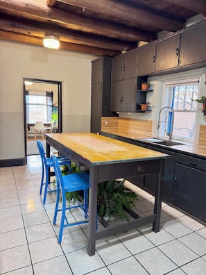 A kitchen with a wooden table, blue chairs, black cabinets, and a window with plants.