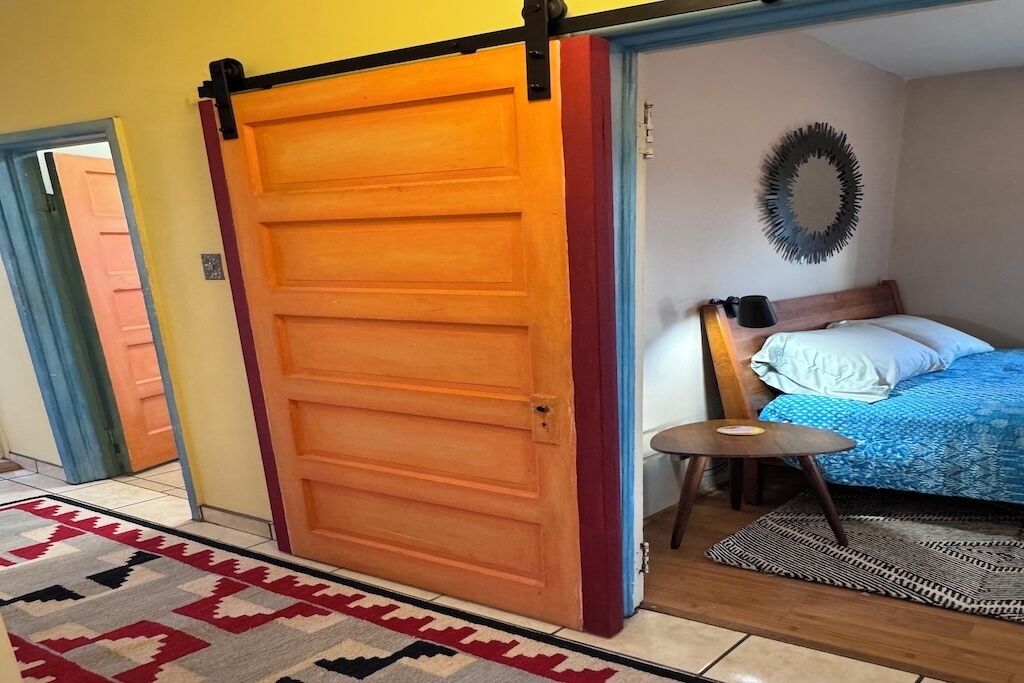 A room with a bed, a small table, a wall-mounted light, and a sliding door.
