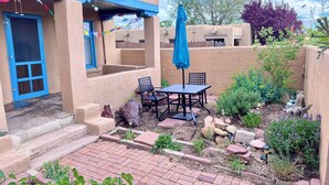 A patio with a table and chairs, a blue umbrella, and a door with blue trim.