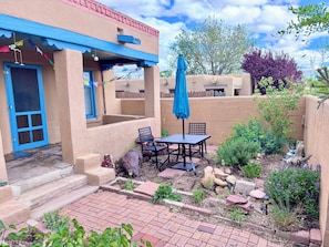 A patio with a table and chairs, a blue umbrella, and a door with blue trim.