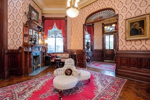 Um quarto com papel de parede estampado, um candelabro, lareira, sofá e um tapete grande.