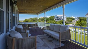 Eine überdachte Veranda mit Korbmöbeln, einem weißen Geländer und Blick auf Häuser im Hintergrund.