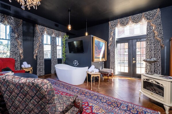 A modern bathroom with a freestanding bathtub, a large mirror, and a television mounted on the wall.
