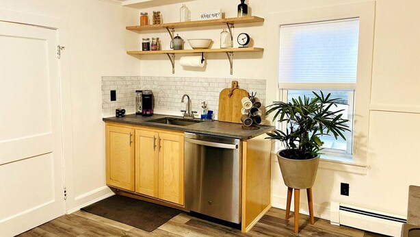 A kitchen with wooden cabinets, a stainless steel dishwasher, a coffee maker, and a potted plant. - Cozy Two Bedroom on Munjoy Hill (Portland)