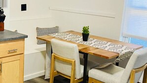 A dining area with a wooden table, two chairs, a potted plant, and framed pictures on the wall. - Cozy Two Bedroom on Munjoy Hill (Portland)
