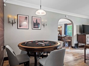 Ein Zimmer mit einem Pokertisch, Stühlen, gerahmten Bildern, Wandleuchten und einem Fernseher.