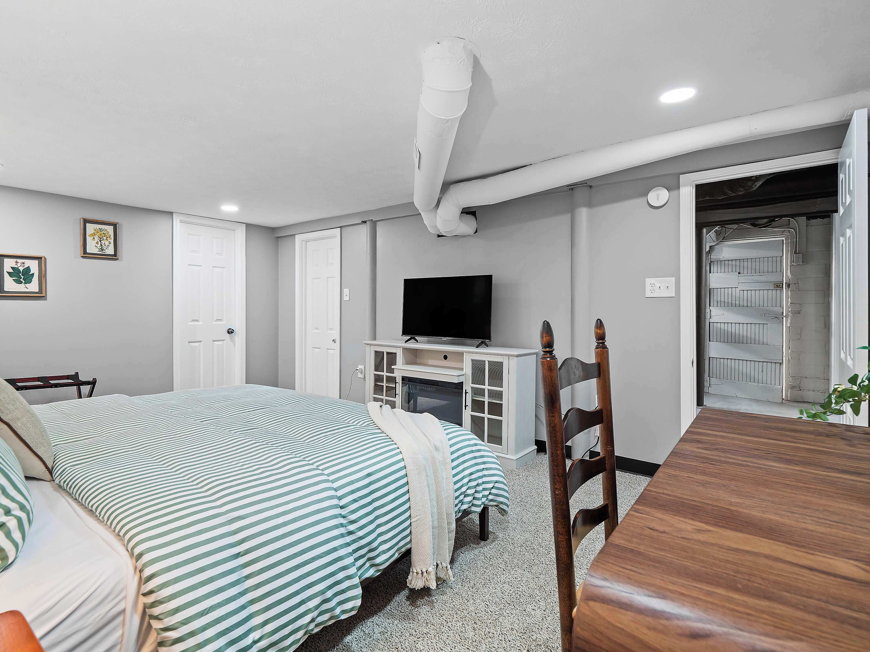 A bedroom with a bed, a TV, a wooden table, and a door leading to another room.