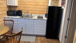 Uma cozinha compacta com armários brancos, uma geladeira preta, um micro-ondas e uma pia.