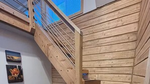 Uma escada de madeira com corrimão de metal, um pequeno aquecedor no chão e duas quadros pendurados na parede.