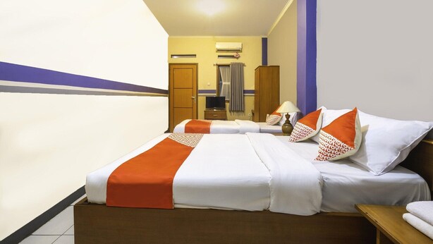 Een hotelkamer met twee bedden, een houten garderobe, een airconditioning en een badkamer op de achtergrond.