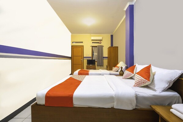 A hotel room with two beds, a wooden wardrobe, an air conditioning unit, and a bathroom visible in the background.