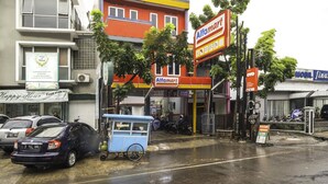 Una calle con un edificio colorido que alberga una tienda Alfamart, un salón de belleza cercano y coches estacionados.