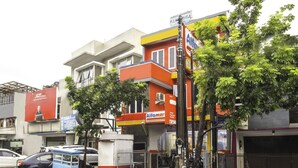 Vista de la calle con un carrito de comida azul, un edificio con una tienda Alfamart y un automóvil estacionado.