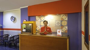 Una recepción con un hombre de camisa naranja, un reloj y una pared decorativa con baldosas estampadas.