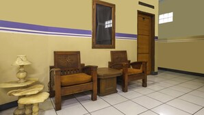Habitación de hotel con sofá de madera, una mesita, una lámpara y una ventana con cortinas.