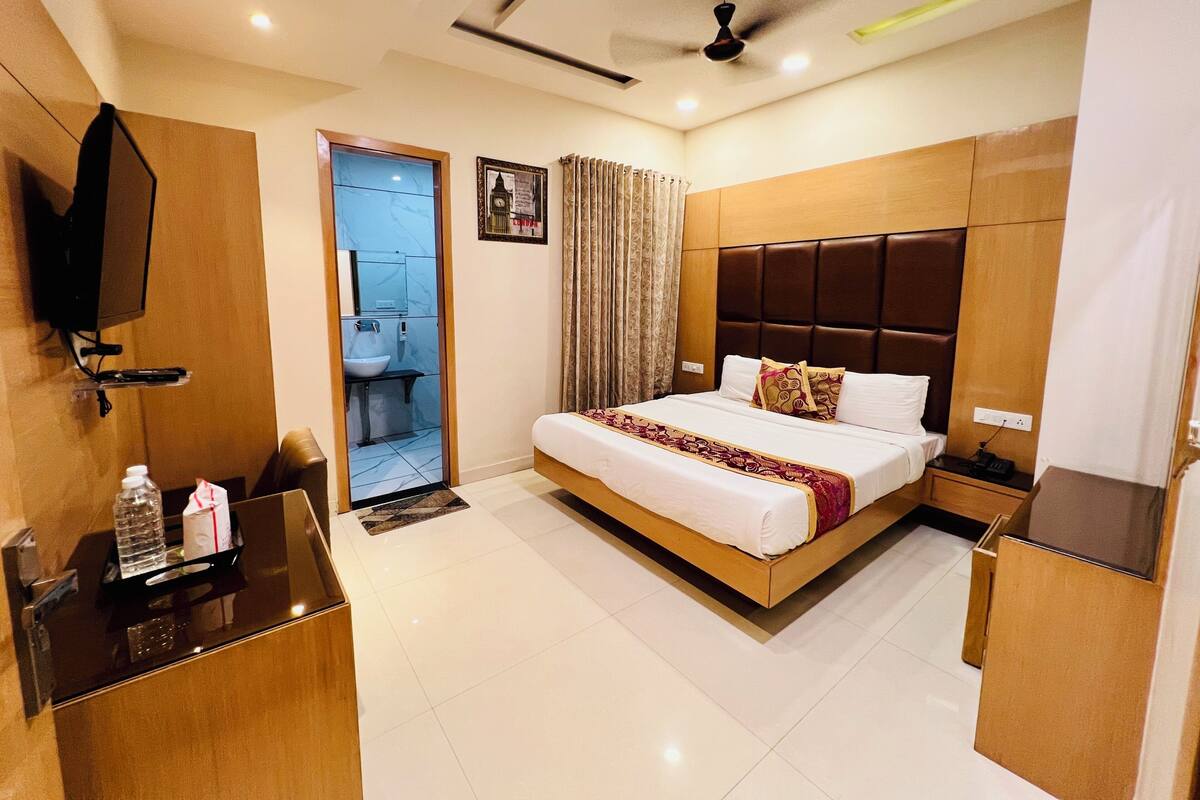 Habitación de hotel con cama, mesita de noche, televisión y baño visible a través de una puerta abierta.