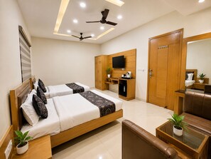 Habitación de hotel con cama, escritorio, silla, armario, televisión y ventiladores de techo.