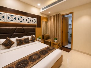 A modern hotel room with a large bed, a wooden headboard, a small seating area, and a view of the bathroom. - THE KING HAWK Nearby GOLDEN TEMPLE (Amritsar)