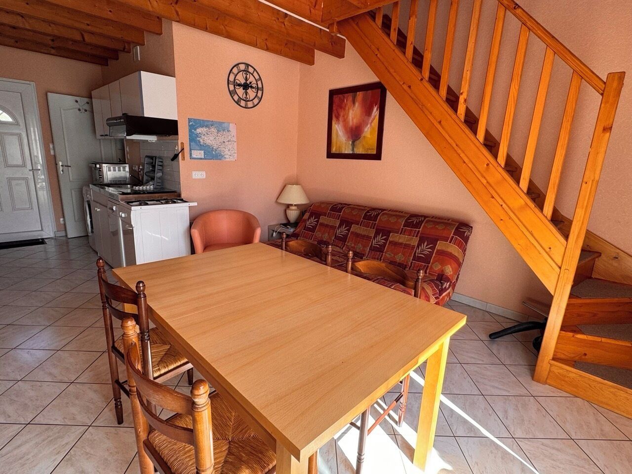 A dining area with a wooden table and chairs, a sofa, a lamp, and a kitchen in the background.
