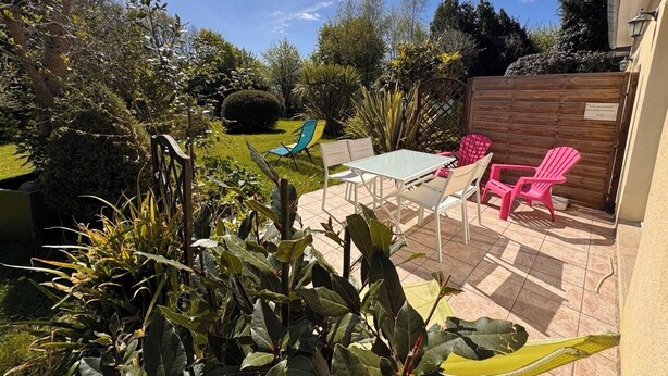 Un patio con mesa y sillas, rodeado de follaje y una valla de madera.