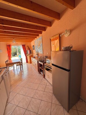 A kitchen with a refrigerator, stove, and dining area with chairs and a table. - Le Pouldu with south-facing garden 5 minutes from the beaches (Clohars-Carnoët)