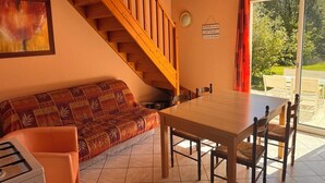 Una habitación acogedora con una escalera de madera, una mesa de comedor con sillas, un sofá y un gran ventanal con vistas a la vegetación.