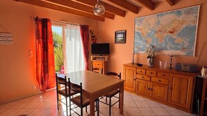 Un comedor con una mesa y sillas de madera, un televisor, un mapa en la pared y un armario con cajones.