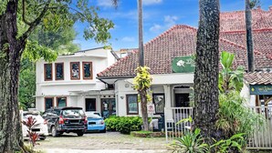 Un edificio bianco con tetto in tegole, auto parcheggiate e vegetazione tropicale.