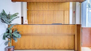 Ein Empfangsschalter mit Holzausstattung, ein Topfpflanze und Schilder, die die Bereiche 'RECEPTION' und 'CASHIER' kennzeichnen.